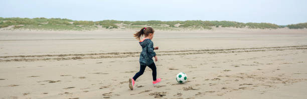 little girl playing soccer on the beach - healthy lifestyle nature sports shoe childhood imagens e fotografias de stock