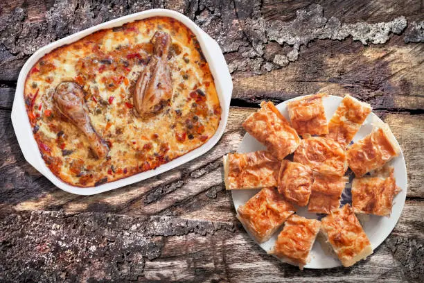 Photo of Plateful Of Freshly Baked Chicken Vegetable Stew And Traditional Serbian Gibanica Crumpled Cheese Pie Served On Old Weathered Cracked Pinewood Picnic Table