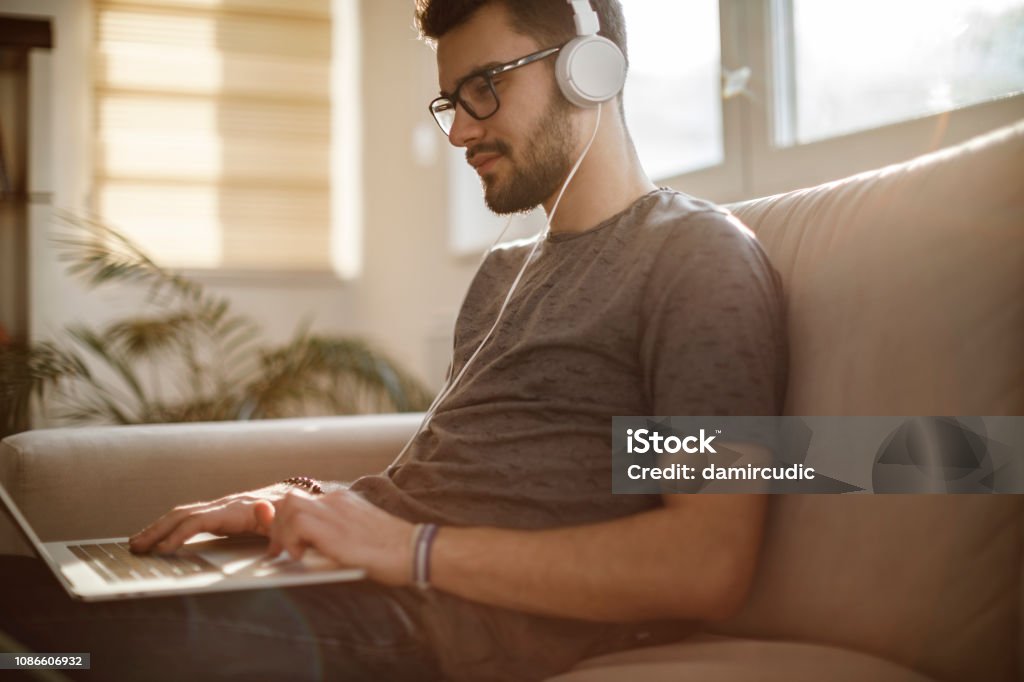 Young man using laptop and listening to music at home Internet Stock Photo