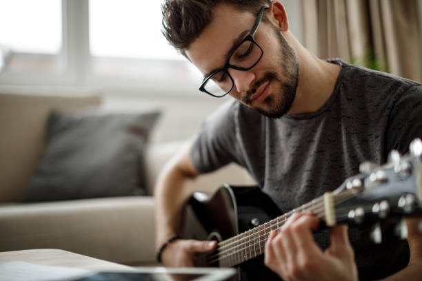 jeune homme jouer de la guitare à la maison - singing lesson photos et images de collection