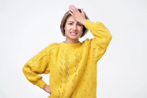 Portrait of excited young woman in yellow sweater holding her head. She has forgotten about her boyfriend birthday