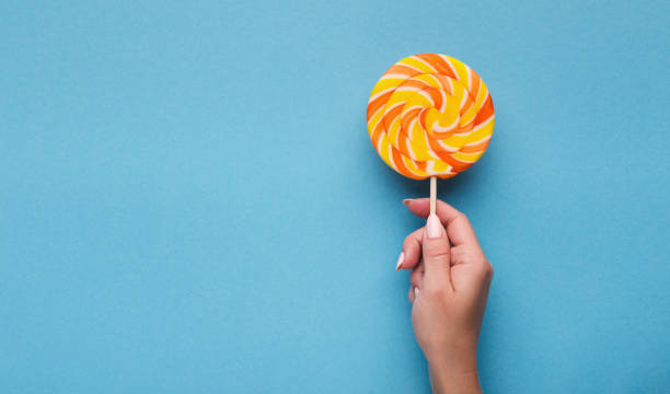 istock Spiral candy lollipop in hand on blue background, top view 1086624108