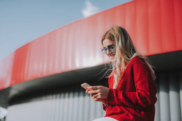 Charming young woman in glasses using cellphone outdoors