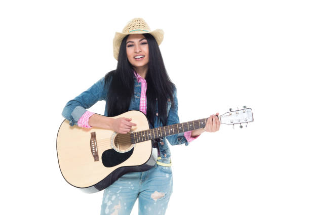 Confidence woman guitarist playing six string acoustic guitar and looking at camera, standing full length. Young adult female musician with glasses is dressed in red leather jacket, jeans and sneakers