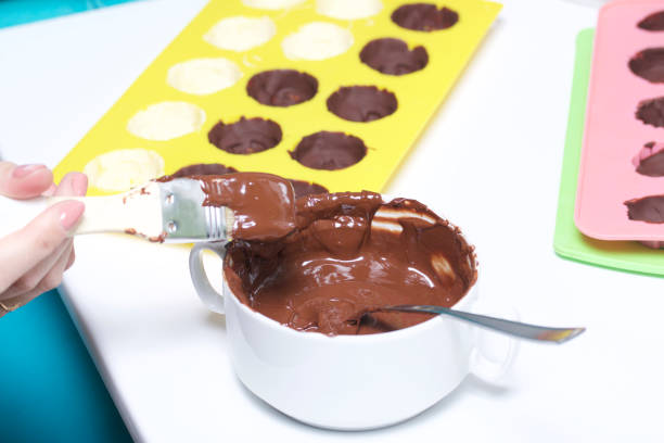 istock A woman using a brush brushes a silicone dessert mold with a melted black chocolate. Nearby are other ingredients. 1086668718