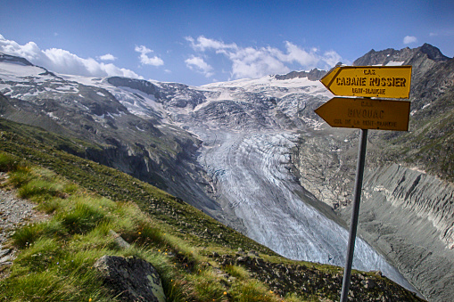 mountain landscape with green fields and snowy peaks and wild glacier in the Swiss Alps and yellow hiking trail signpost in the Zinal Valley in the Valais in Switzerland
