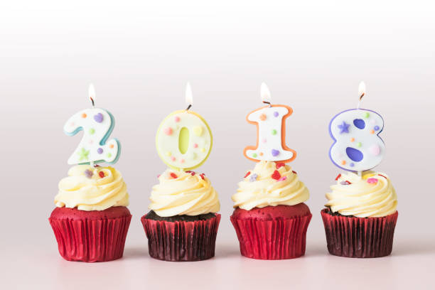 istock 2018 Happy New Year Cupcakes with candle lit light isolated with clipping path on white and pastel pink table background 1086725322