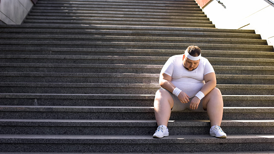 Fat man sitting on stairs after jogging, no faith in himself, insecurities