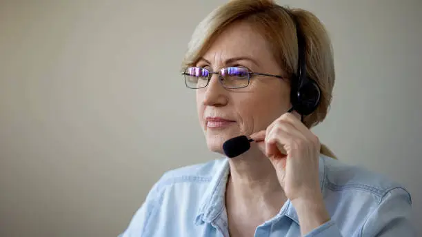 Attractive senior lady with headset consulting travel agency clients, services