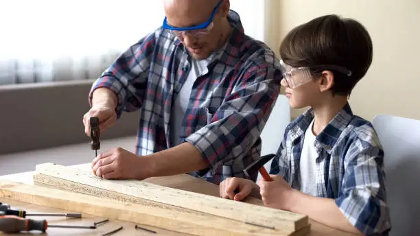 Dad teaching little son how to use hammer safely, family leisure, hobby and fun