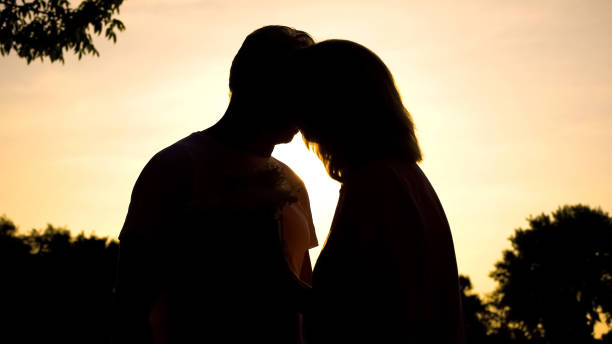 elderly couple kissing at sunset, romantic moment, love feeling, happiness - silhouette kissing park sunset imagens e fotografias de stock