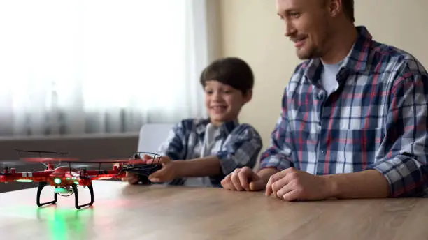 Joyful boy and his father operating quadcopter at home, leisure time, device