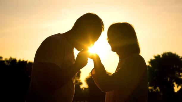 silhouette of gentleman kissing wife's hand, senior couple in love, romance - silhouette kissing park sunset imagens e fotografias de stock