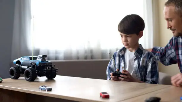Cute kid and his father operating radio controlled car at home, technologies