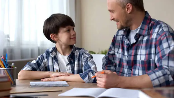 Male kid and father doing homework together, smiling to each other, teamwork