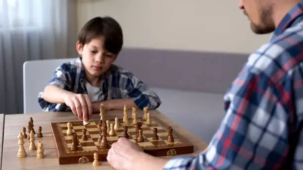 Little son playing chess with father at home, leisure activity, childhood hobby
