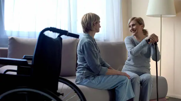 Happy disabled mother talking with middle aged daughter, family relationship