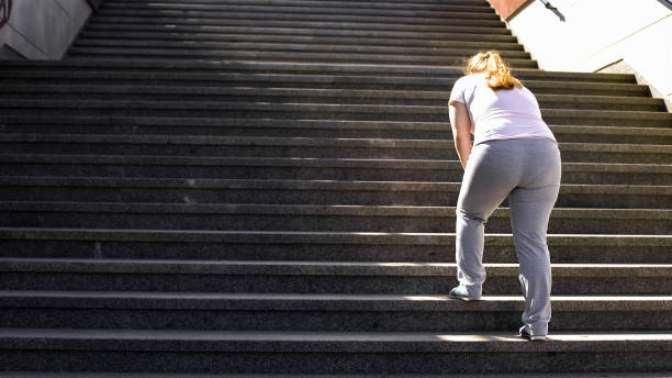 Hard to climb stairs for obese girl, victory over fatigue for goal achieving Hard to climb stairs for obese girl, victory over fatigue for goal achieving patience photos stock pictures, royalty-free photos & images