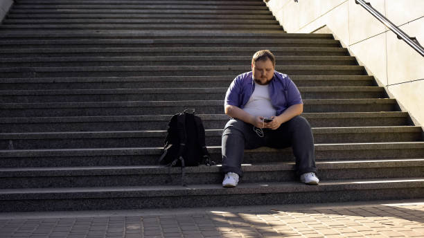 uomo grasso che ascolta musica sulle scale, solitudine, sovrappeso causa insicurezze - weight scale dieting weight loss foto e immagini stock