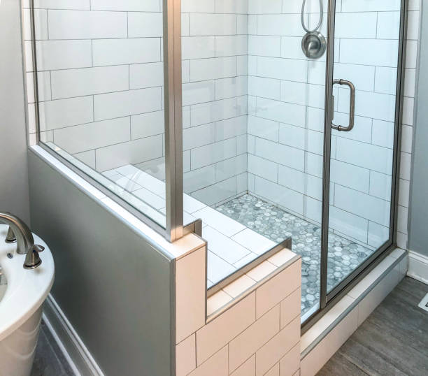 istock Bathroom shower base with white rectangular wall tiles, custom shower seat, mosaic floor tiles inside shower base and brownish floor tile. Glass shower doors and panels with chrome bathroom fixtures 1086734494