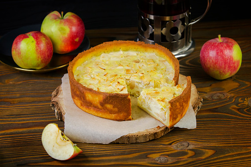 Apple cheesecake on a rustic kitchen with a tea kettle on the wooden dark background.