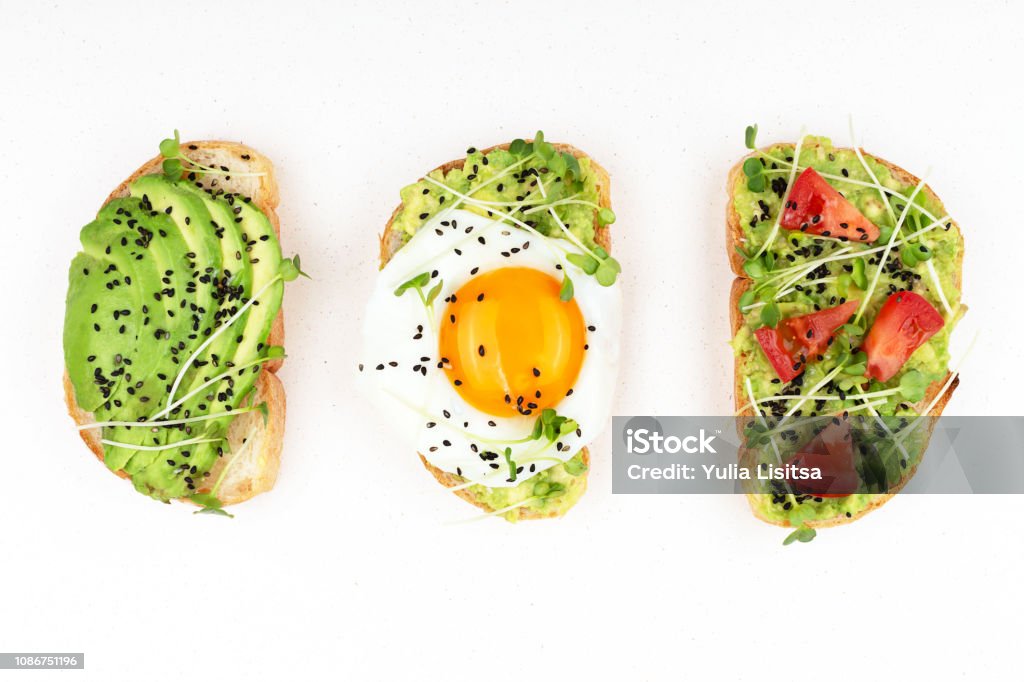 Three healthy toasts Three healthy toasts with egg, avocado, micro greens and tomatoes. Breakfast or healthy eating concept, plant based food. Flat-lay, top view. Avocado Stock Photo