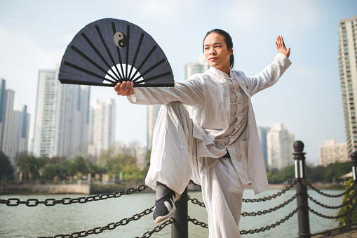 Young man practicing tai chi with folding fan in the park in the morning