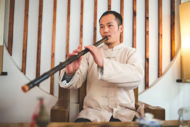 Young man playing xiao, traditional bamboo flute indoors.