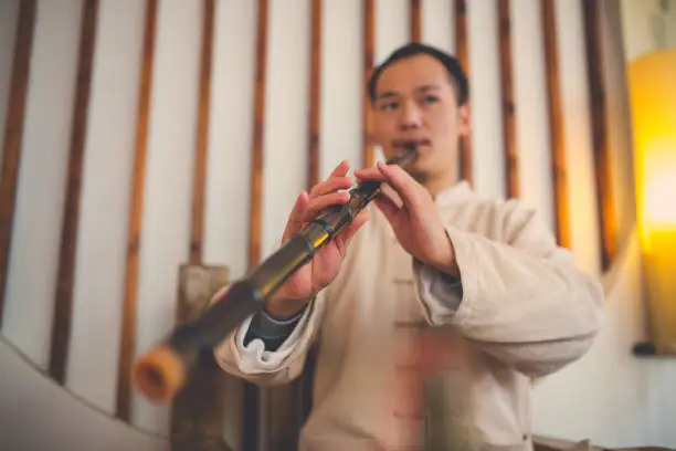 Young man playing xiao, traditional bamboo flute indoors.