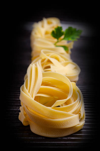 Traditional dry fettuccine pasta on dark wooden background. Selective focus.