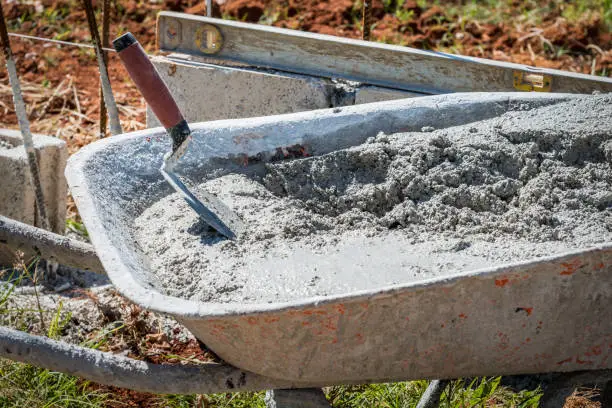 Mixed wet cement in wheelbarrow with red handle trowel dipped in it on a construction site