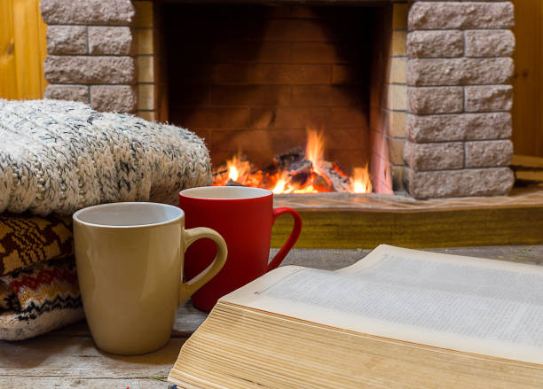 istock Cozy scene before fireplace with two big mugs with tea, opened book and wool scarf. 1086808708