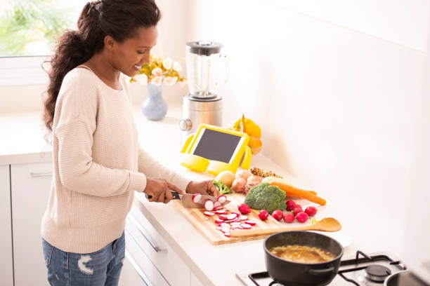 istock Woman chopping radish, preparing food, cooking vegetable soup, using a tablet computer to see the recipe. 1086812832