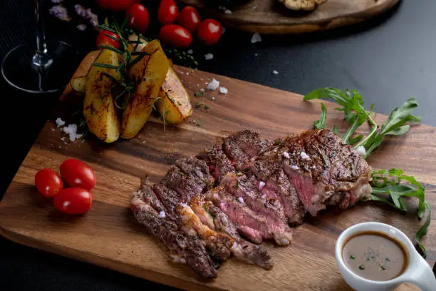 Medium rare meat rib eye steak slices in pan on chopping wooden board served with beef sauces look delicious. American style food.