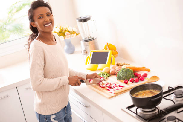 istock Woman chopping radish, preparing food, cooking vegetable soup, using a tablet computer to see the recipe. 1086826994