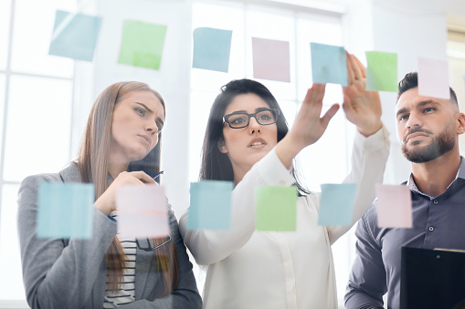 Employees sticking reminders on visualization board with business tasks and deadlines in office