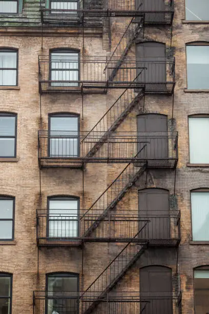 Photo of Fire escape stairs and ladder, in metal, on a typical North American old brick building from the Old Montreal, Quebec, Canada. These stairs, made for emergency, are symbolic of the architecture