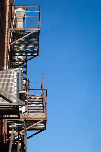 Photo of Fire escape rusty stairs and ladder, in metal, on a typical North American old brick building from Montreal, Quebec, Canada. These stairs, made for emergency, are symbolic of the architecture