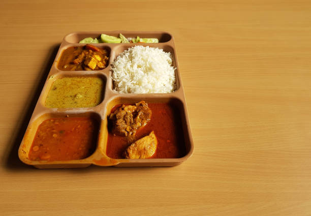 indian chicken thali with rice dal chicken salad vegetable curry on a plastic segmented plate in wooden background