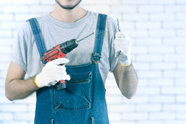 Man is holding drill with two hands wearing white gloves ready to work, DIY concept.