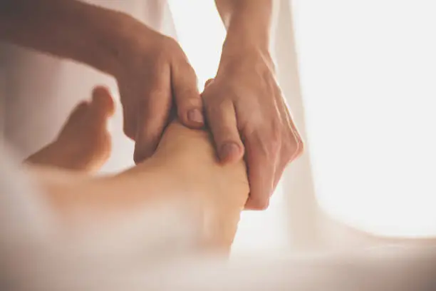 Close-up shot of massage therapist doing foot massage to client at spa.