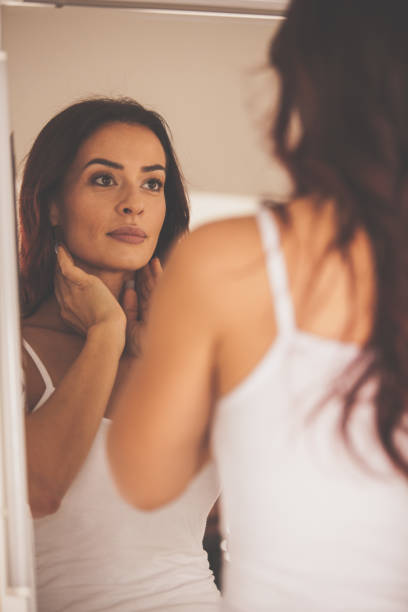 woman looking at her reflection in the mirror - mirror women looking reflection imagens e fotografias de stock