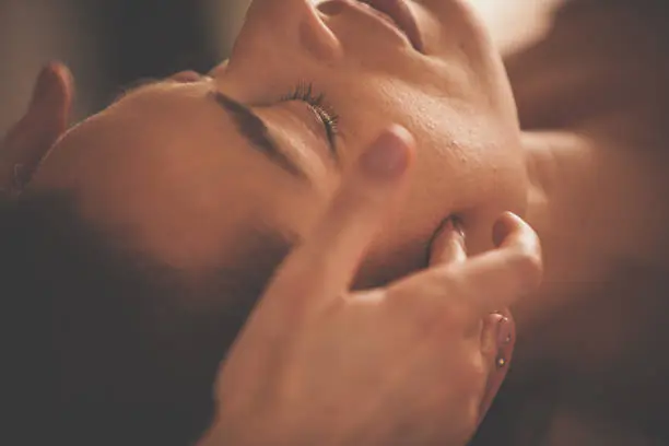 Close-up shot of a mid adult woman relaxing with eyes closed during head massage at spa.