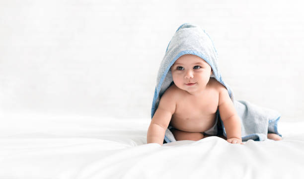 Adorable baby wearing hooded towel after bath Bedding time. Adorable baby wearing hooded towel after bath crawling on bed, copy space young hot stock pictures, royalty-free photos & images