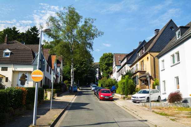 View uphill street with single and double houses in Essen Kettwig. Some cars are parked in street. Name of street is Prälatenweg.