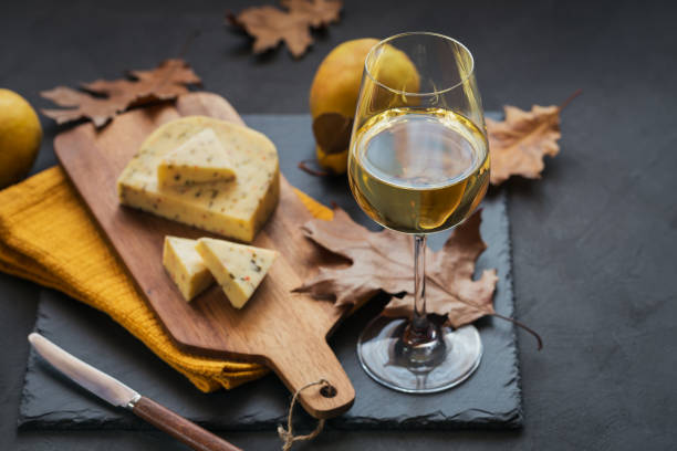 a glass of white wine served with cheese in a cutting board on dark background - gouda imagens e fotografias de stock