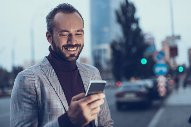 istock Pleased man smiling while looking at the screen of modern device 1086873234