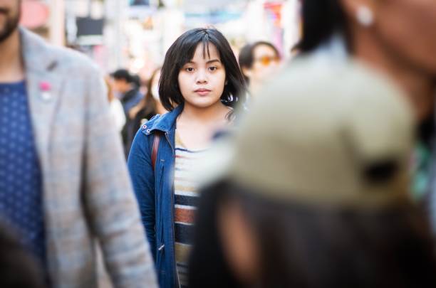 Alone in a crowd A young woman standing in the middle of a crowded street, looking at the camera. crowded stock pictures, royalty-free photos & images