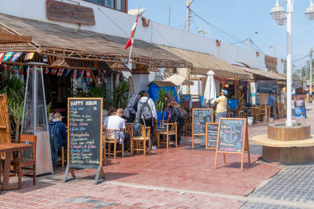 People sitting on chairs outside a restaurant in Pisco, Peru. Seen during sunny day in the summer.