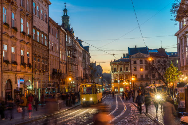 Lviv, Ukraine - October 31, 2018:  view showing people walking around Lviv Old town square, building apartments, trams in the tramway and church tower can be seen on the background at night